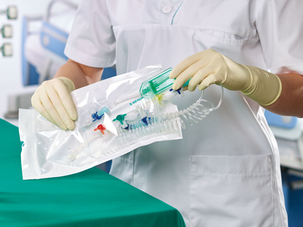 Medizinische Fachkraft mit Handschuhen wickelt steriles Spiralschlauchset für Infusion aus