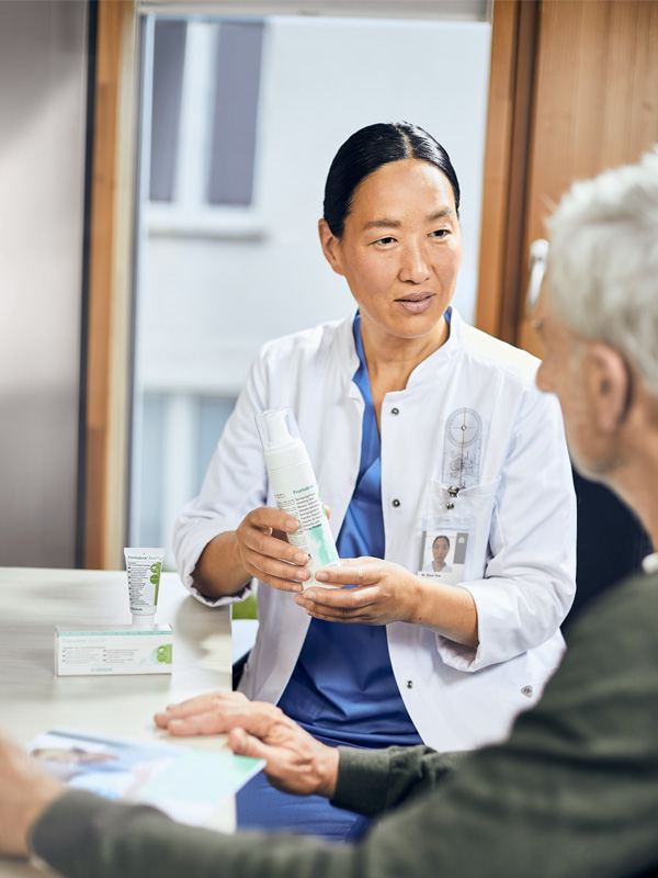 Ärztin zeigt einem älteren Patienten Prontodermenschaum